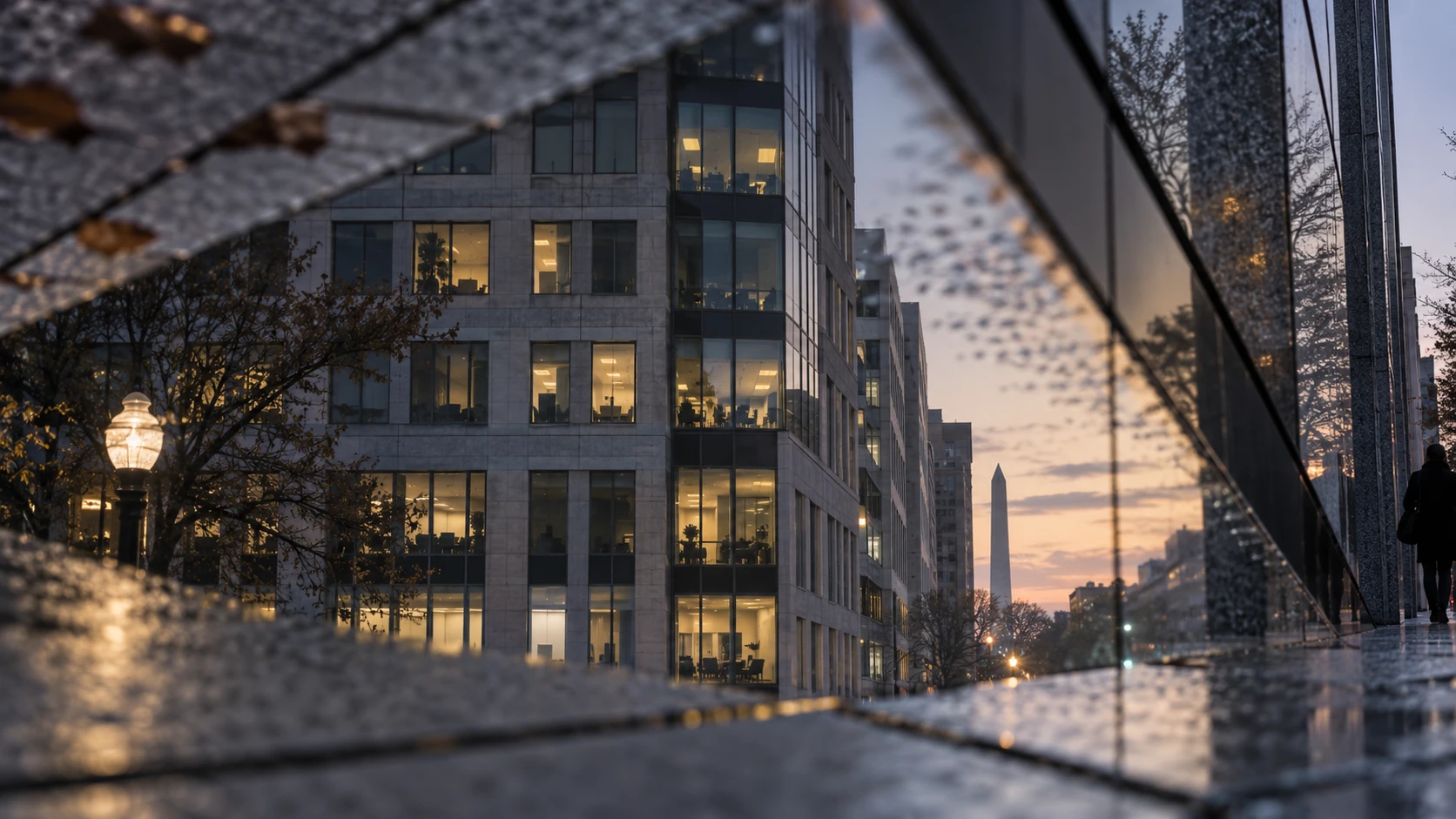 Office building glass façade at dusk reflecting raindrops, neighboring towers and a street lamp, one pedestrian passing.